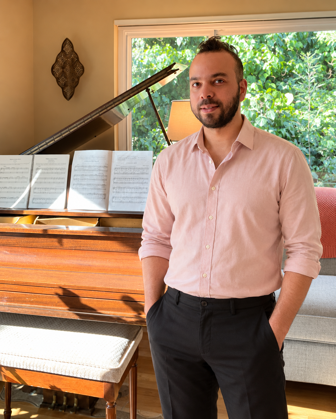 Mahdiar Sadeghi standing beside a piano in a sunlit room.